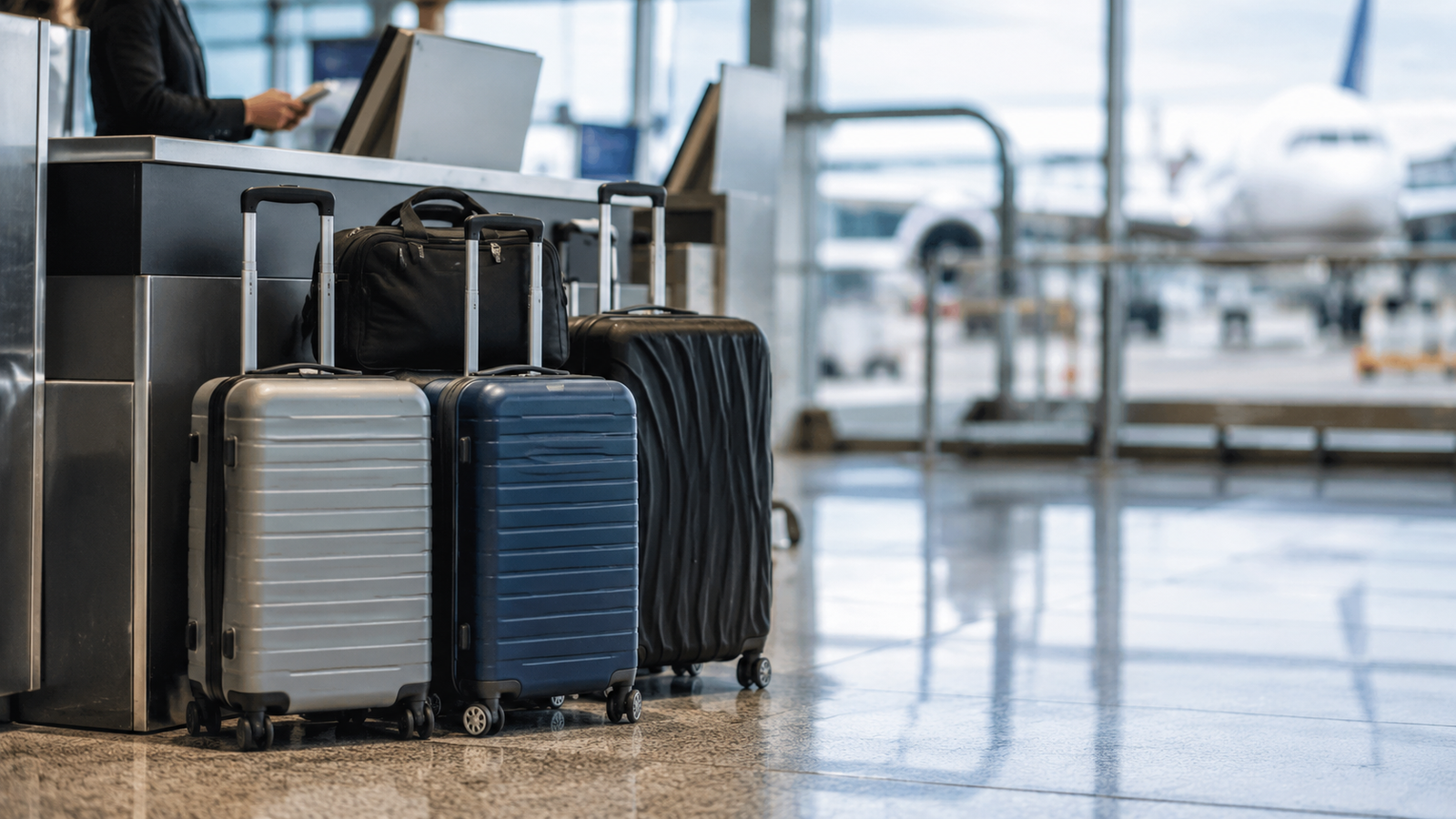 Koper bagasi berada di area check-in bandara dengan pesawat terlihat di latar belakang