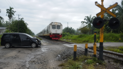 Perlintasan rel kereta tanpa palang di kawasan permukiman dengan rambu peringatan terlihat jelas