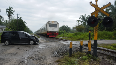 Perlintasan rel kereta tanpa palang di kawasan permukiman dengan rambu peringatan terlihat jelas
